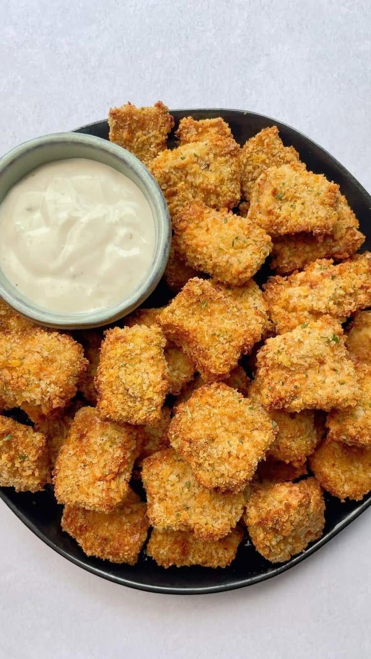 Breaded tofu nuggets on a black plate with a side of white dipping sauce.