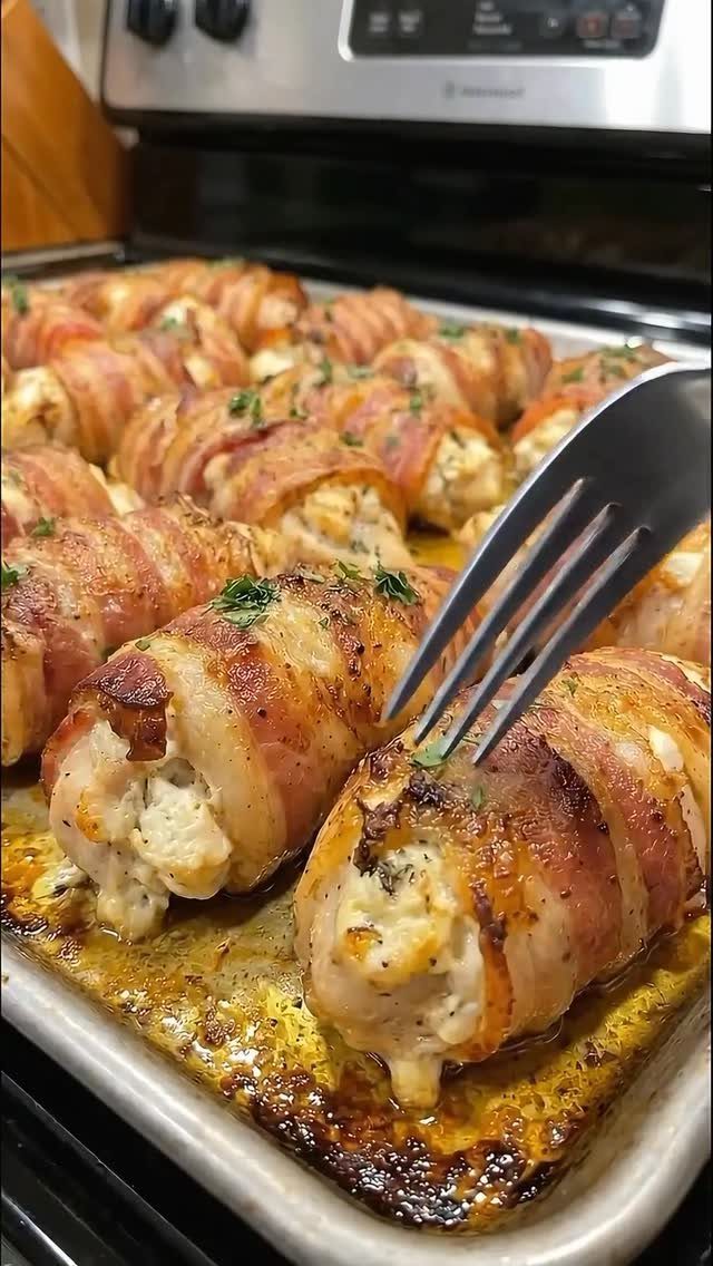 Bacon wrapped stuffed chicken breasts baked on a tray with a silver fork.