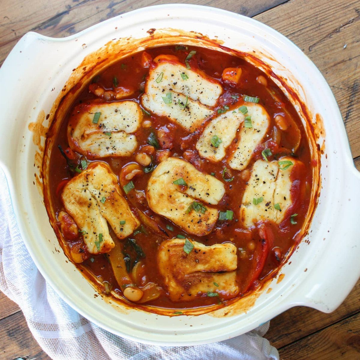 Bean and halloumi stew in a white pot with seared cheese and herbs.