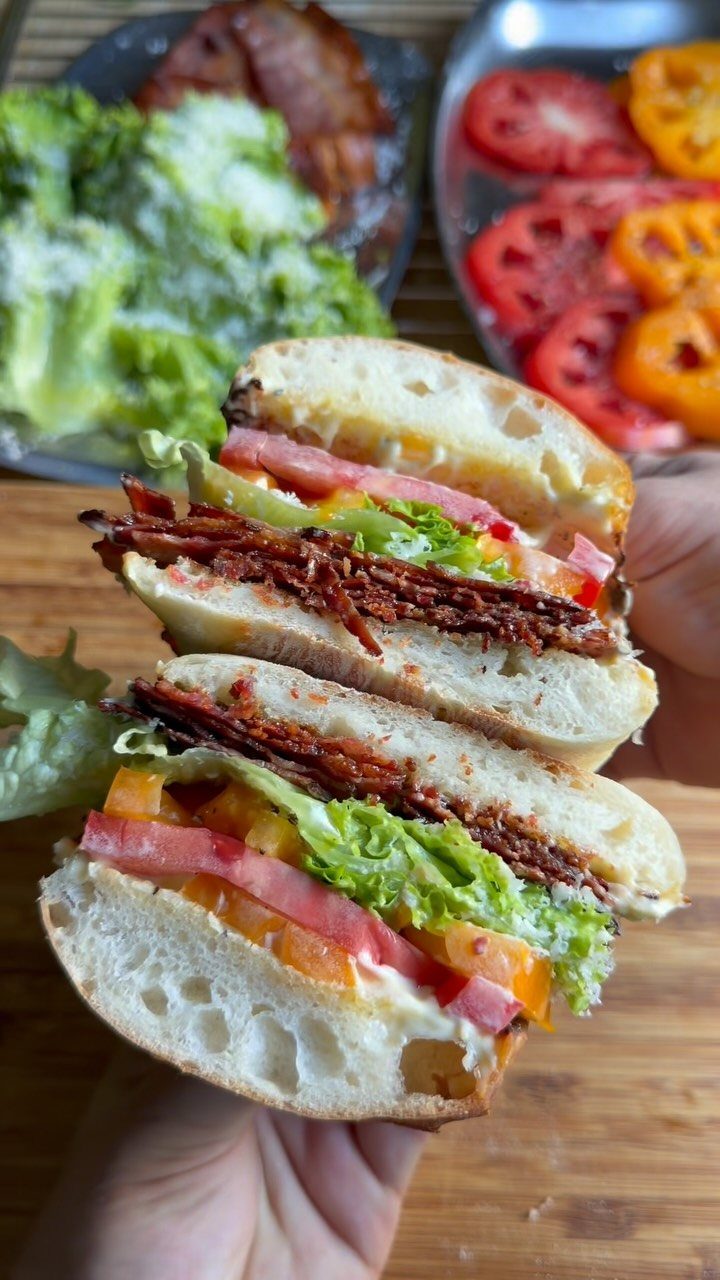 Toasted BLT sandwich halves with bacon, lettuce, and tomato held over wooden table.