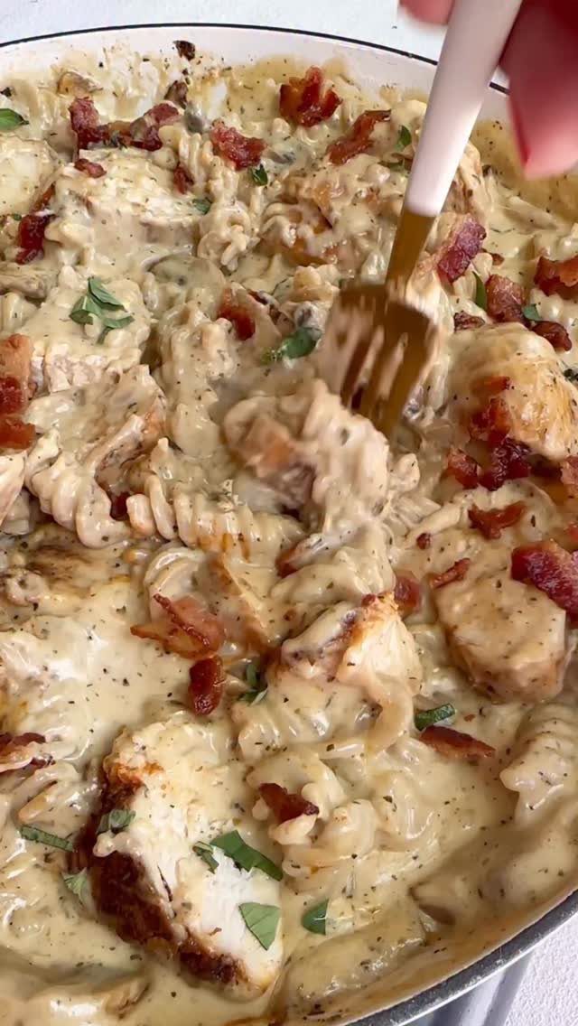 Creamy rotini pasta with chicken and bacon bits in a white skillet pan.