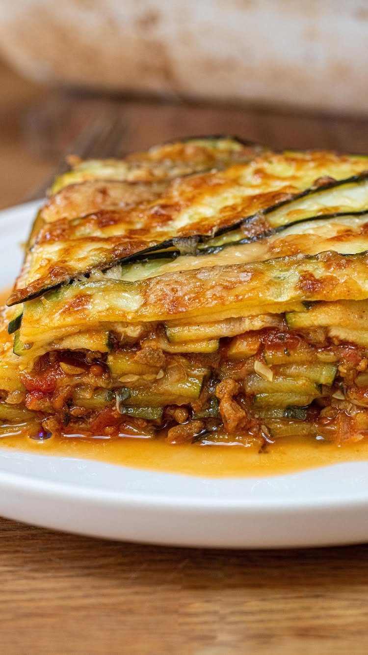 Zucchini lasagne slice with melted cheese and tomato sauce on a white plate.