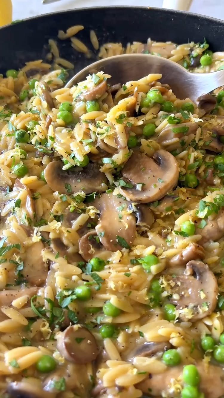 Creamy orzo pasta with sliced mushrooms, green peas, and fresh herbs in a pan.