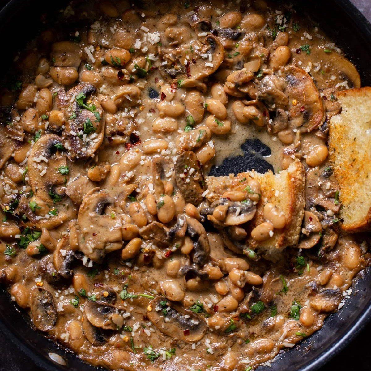 Creamy mushroom and white bean stew in a pan with toasted bread.