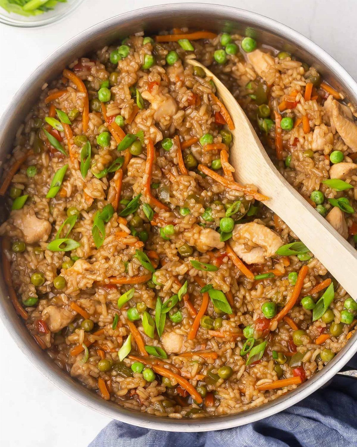 Chicken fried rice with peas and carrots in a pan with a wooden spoon