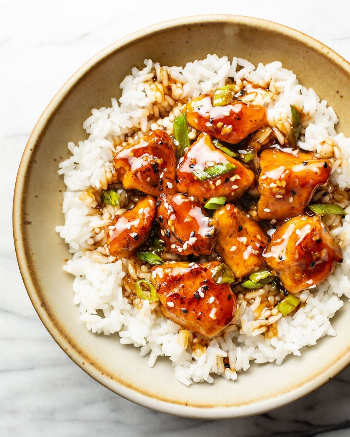 Glazed teriyaki chicken with sesame seeds and green onions over white sticky rice.
