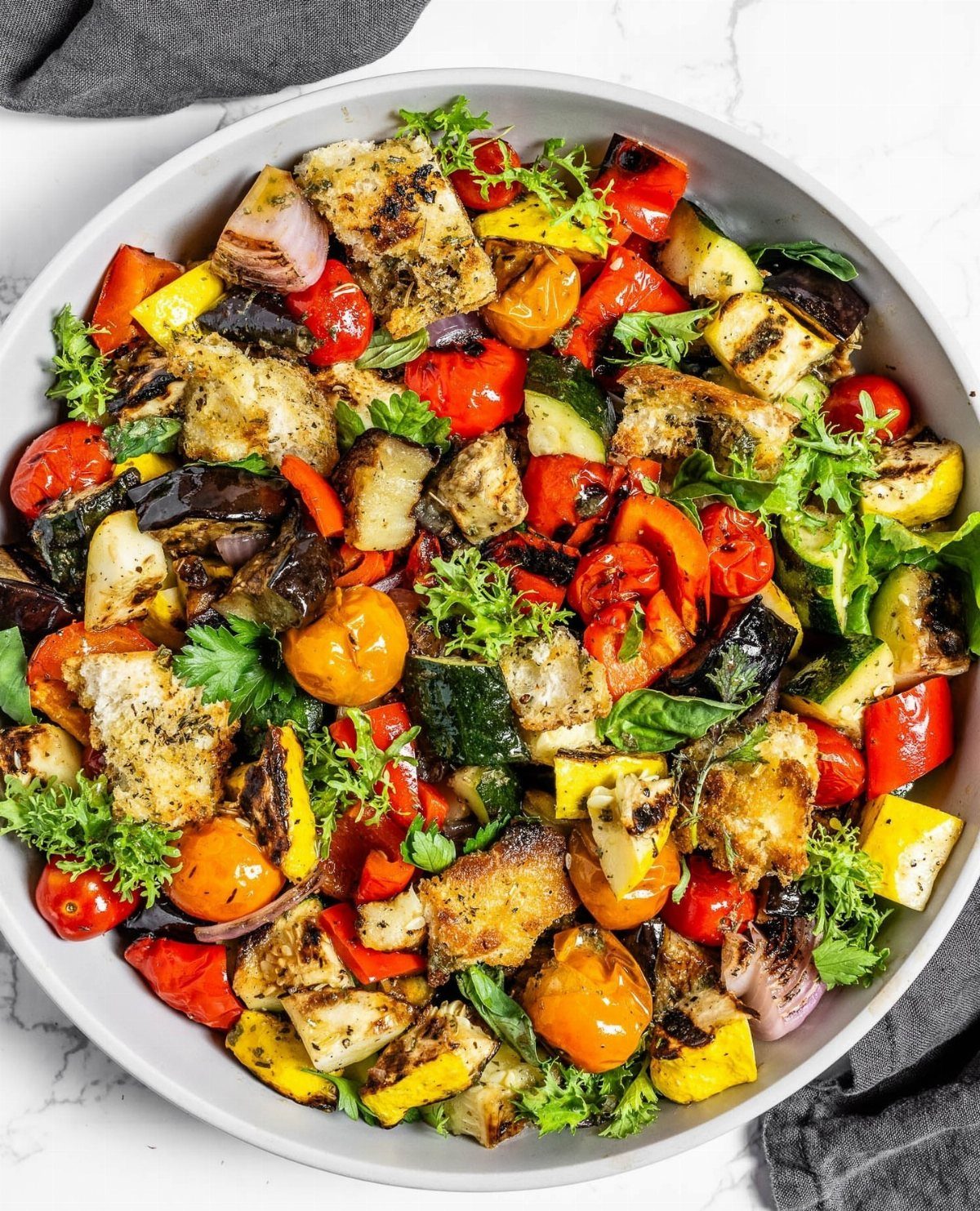 Grilled vegetable salad with charred croutons, zucchini, and peppers in a white bowl.