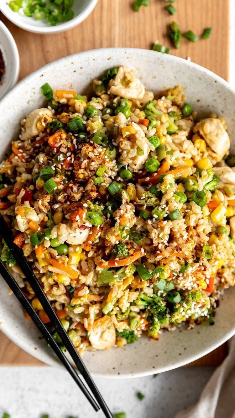 Chicken fried rice with mixed vegetables and sesame seeds in a white bowl.