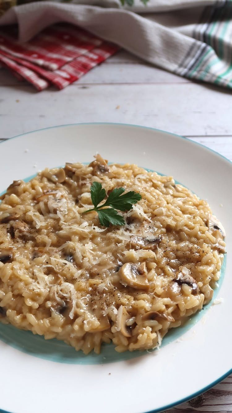 Creamy mushroom risotto topped with grated cheese and a parsley leaf on a plate.