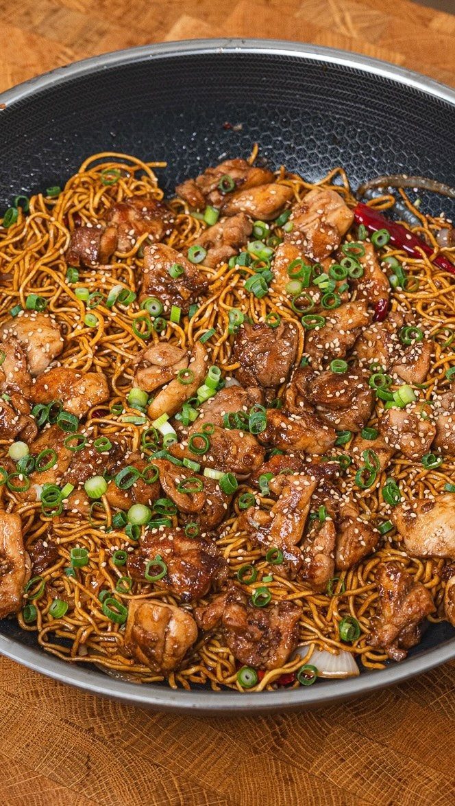 Chicken lo mein noodles with green onions and sesame seeds in a black wok.