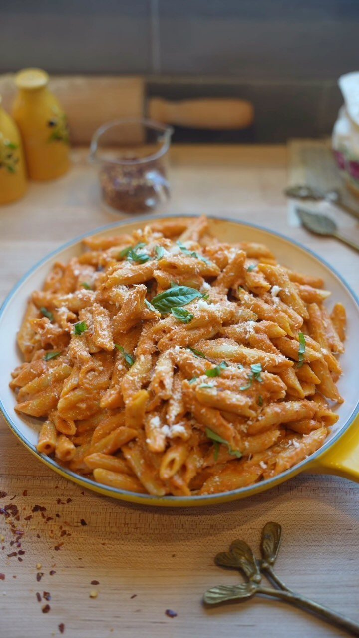 Penne pasta in creamy tomato sauce with basil and cheese in a yellow skillet.