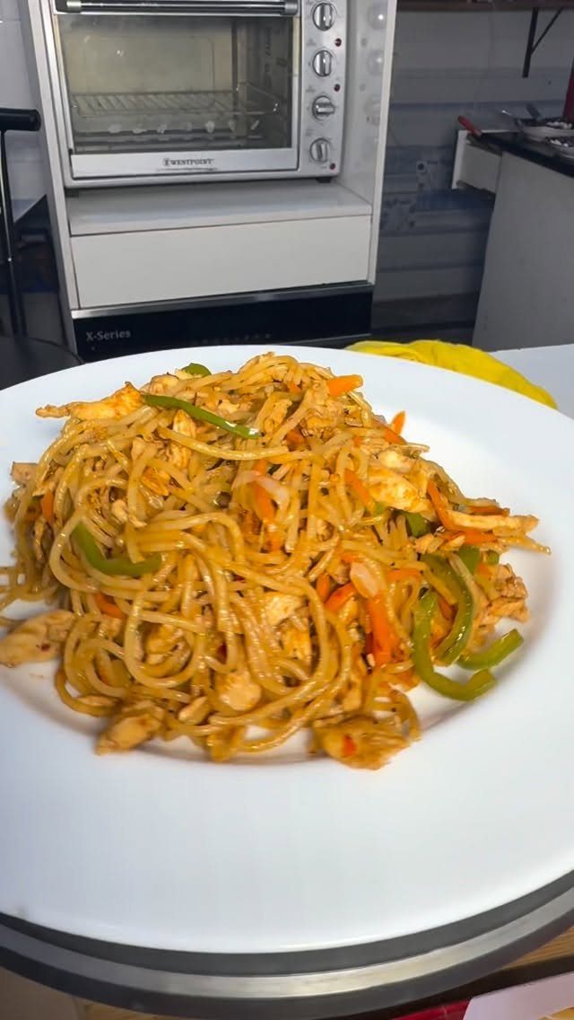 Stir-fried noodles with meat, green peppers, and carrots on a white plate.
