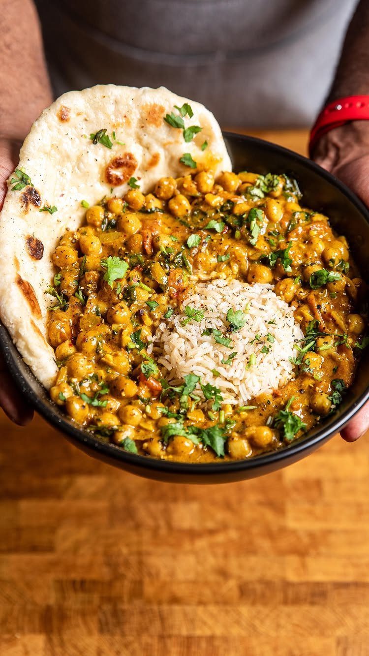 Chickpea curry with white rice and naan bread held in a black bowl.