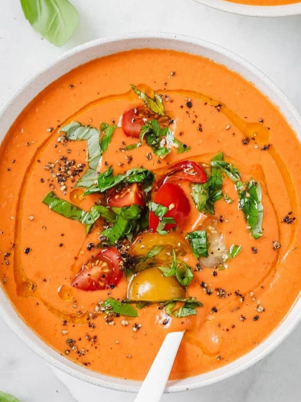 Orange-red gazpacho soup topped with cherry tomatoes, fresh basil, and olive oil.