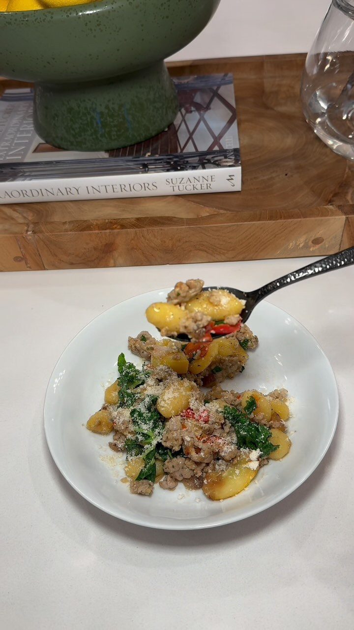 Gnocchi with sausage and kale in a white bowl with a fork lifting some.