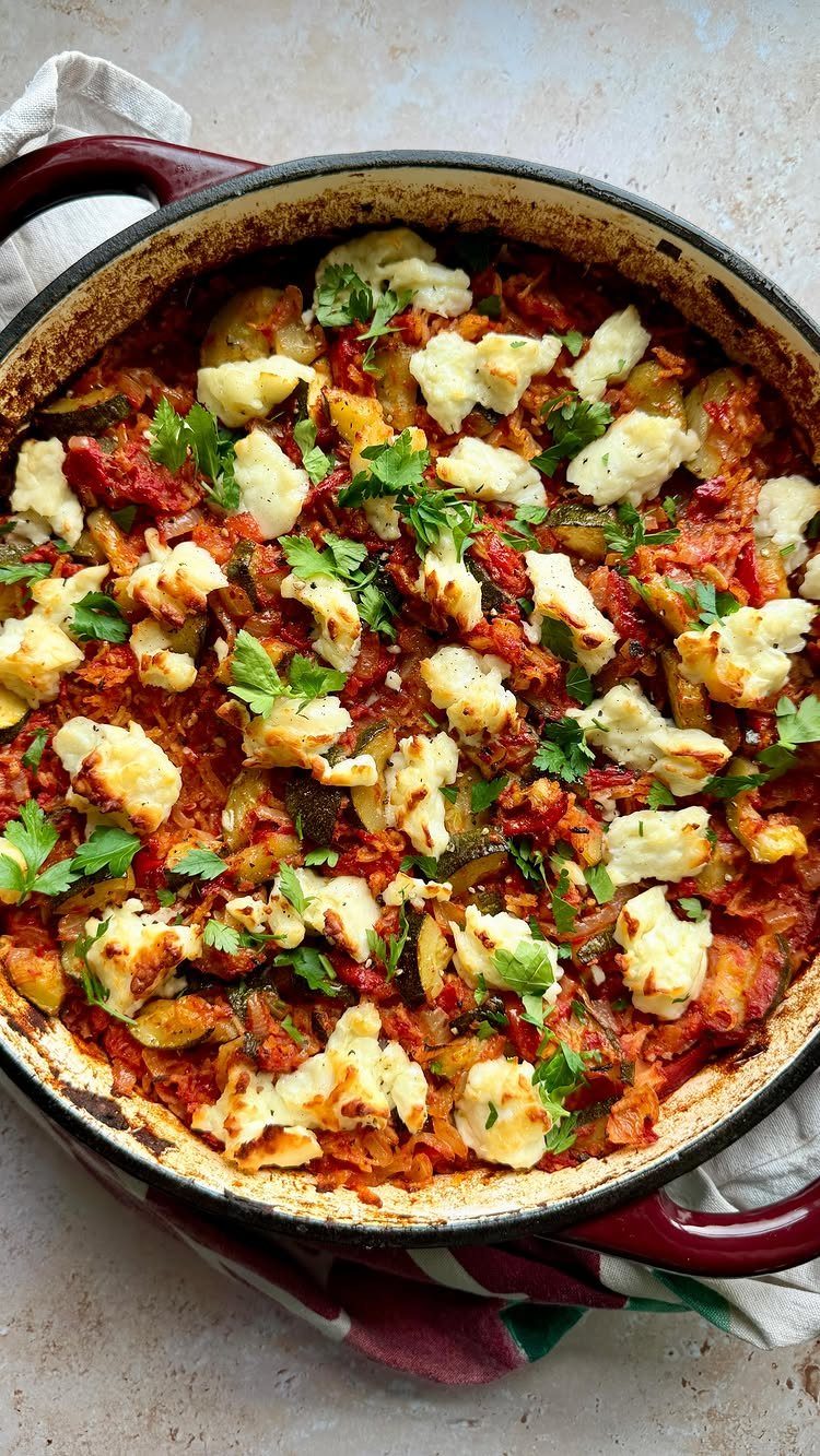 Reddish-orange rice dish with grilled halloumi cheese and parsley in a red pot.