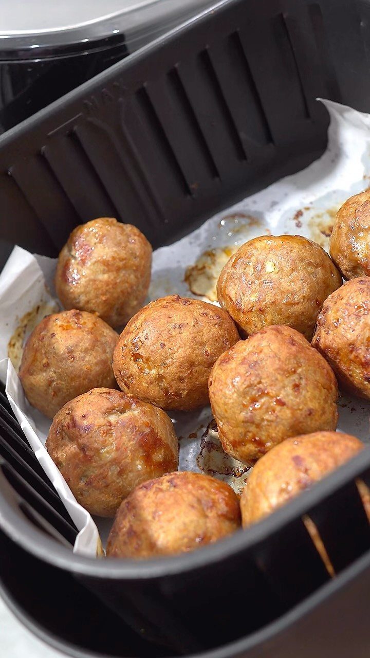 Browned meatballs cooked on parchment paper inside a black air fryer basket.