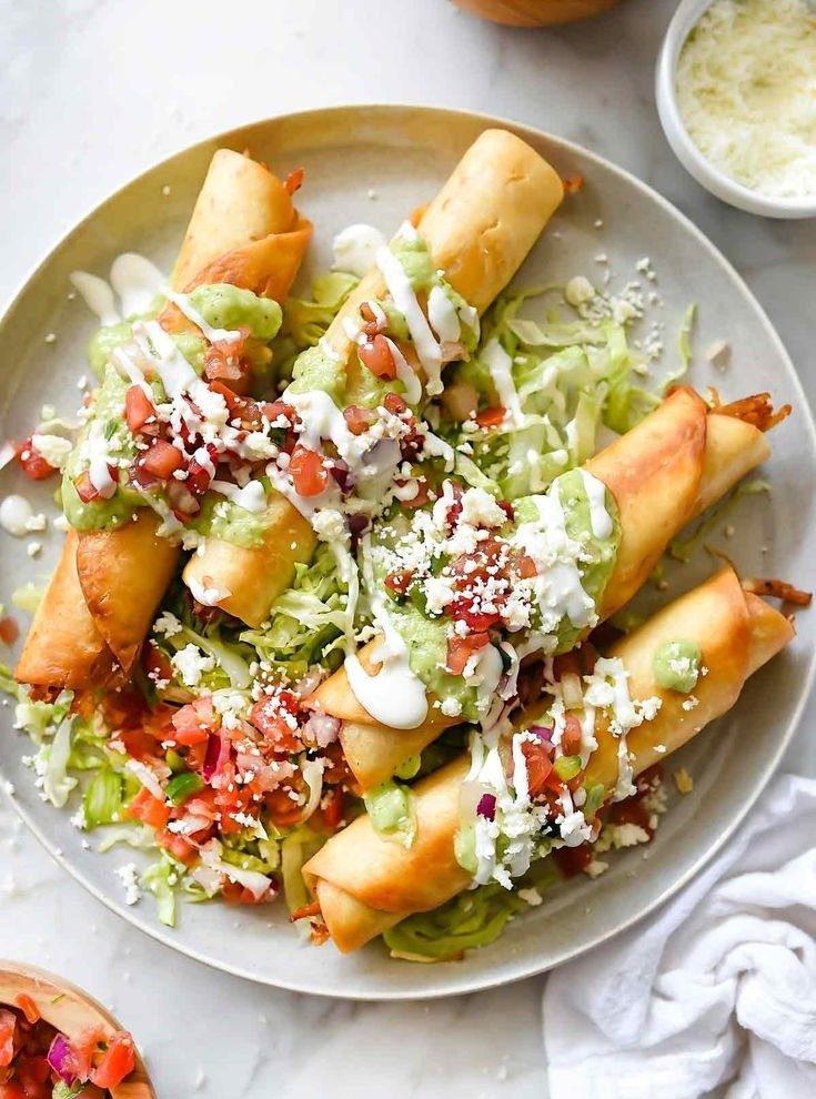 Crispy rolled taquitos topped with guacamole, crema, and pico de gallo on a plate.