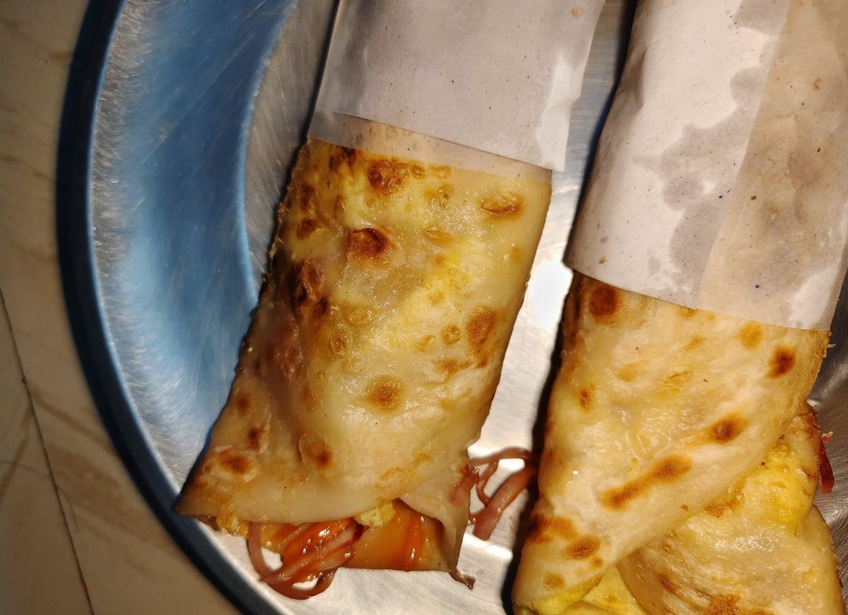 Two toasted flatbread wraps filled with eggs and vegetables on a blue plate.