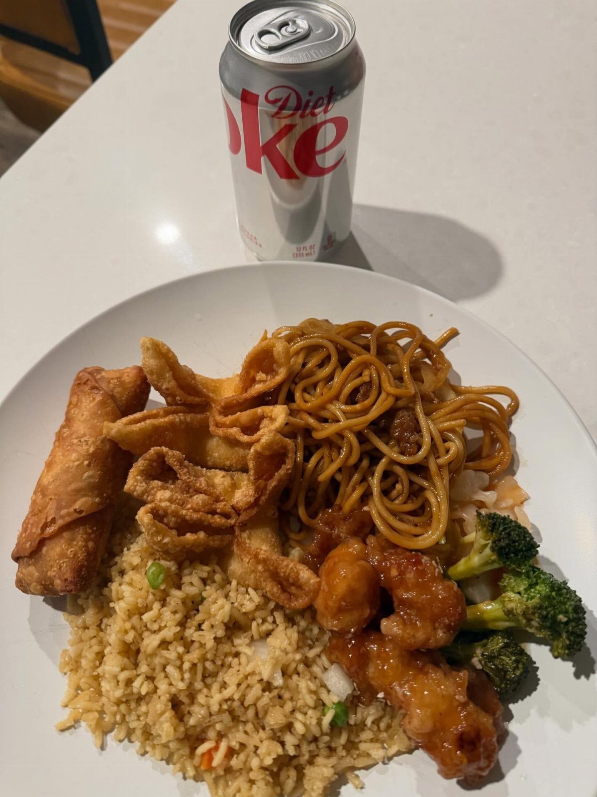 Chinese takeout platter with fried rice, noodles, orange chicken, and a soda can.