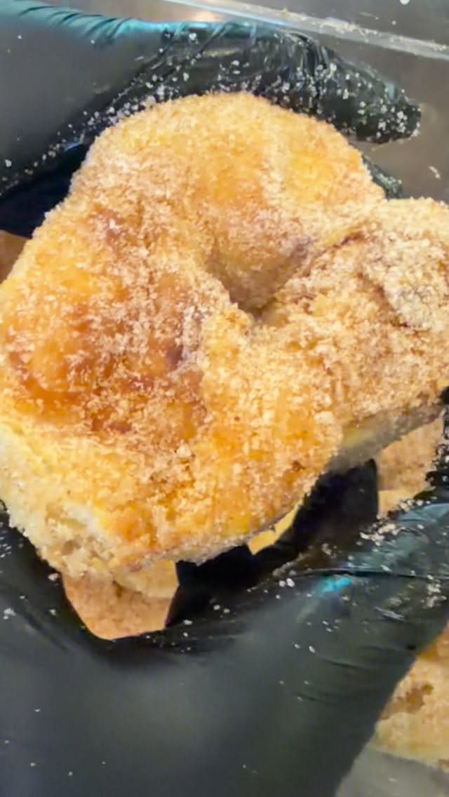 Cinnamon sugar coated donut held by a person wearing black gloves.