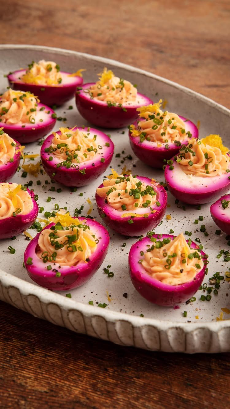 Pink deviled eggs with creamy filling and chives on a white platter.