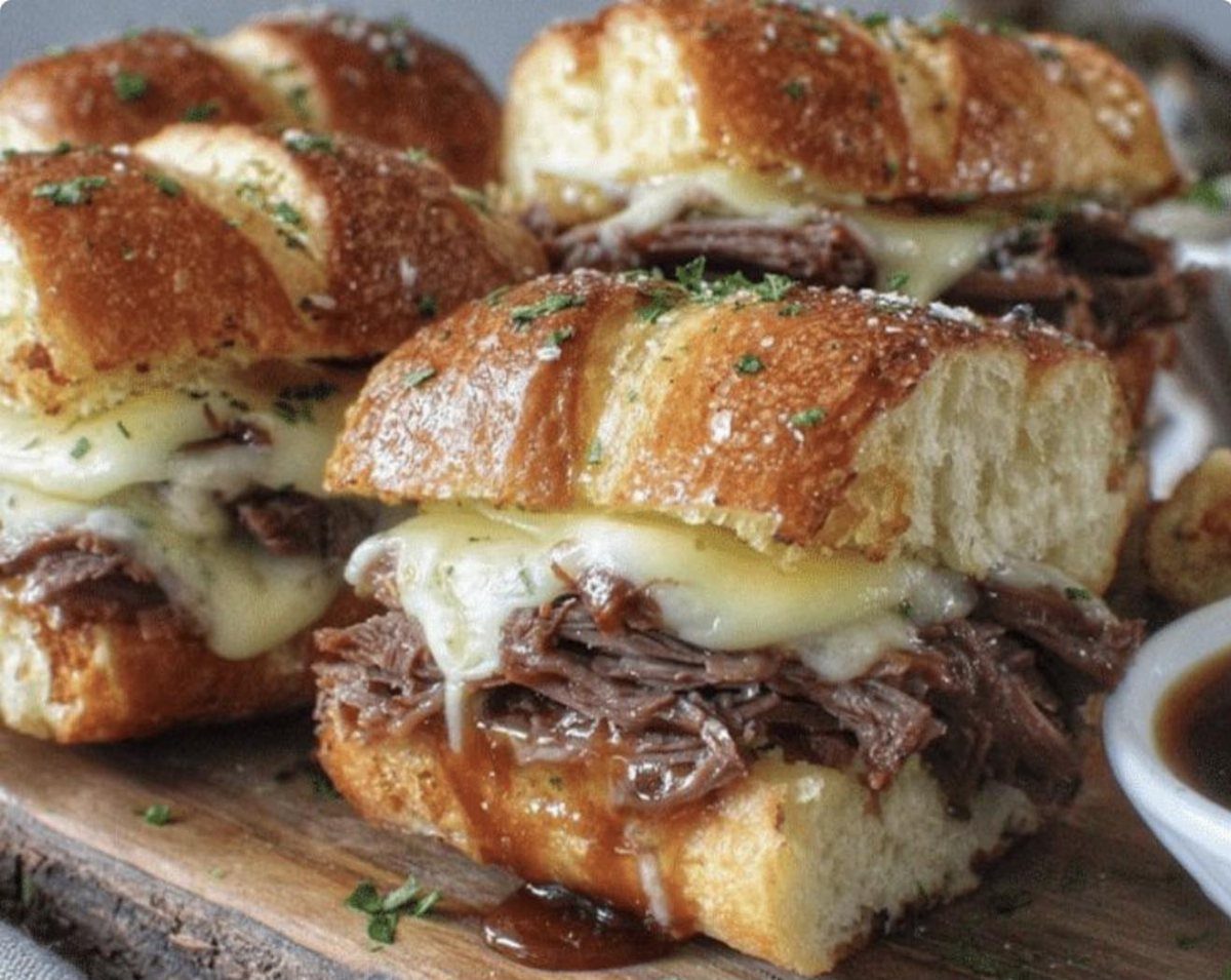Toasted baguette sandwiches with shredded beef and melted cheese on a wooden board.