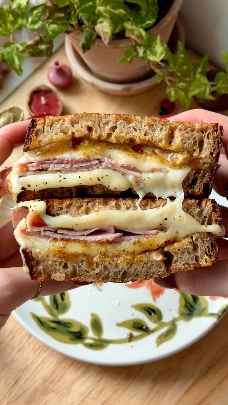 Toasted ham and cheese sandwich held over a decorative white ceramic plate.