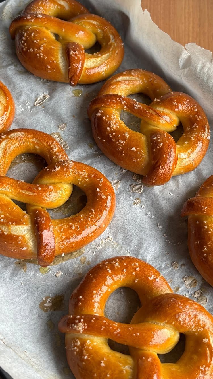 Golden-brown salted soft pretzels resting on white parchment paper on a baking sheet.