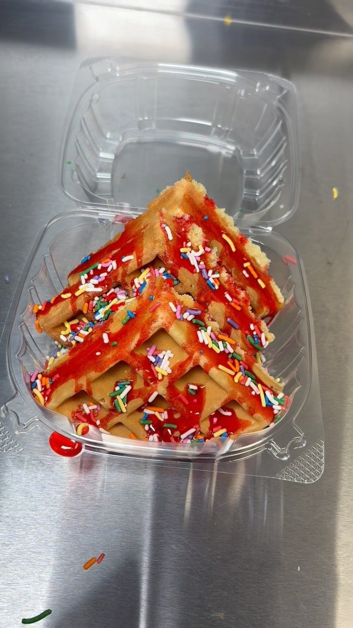 Mini triangular waffle with red syrup and colorful sprinkles in a plastic container.