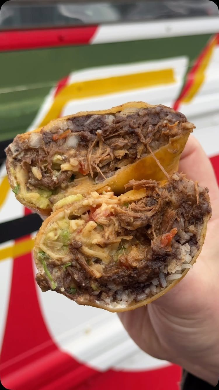 Half of a loaded burrito with meat, rice, and guacamole held in hand.