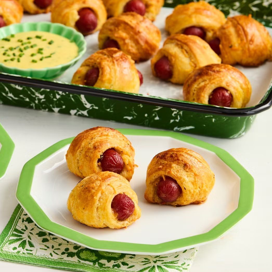 Pigs in a blanket served on a green plate with dipping sauce.