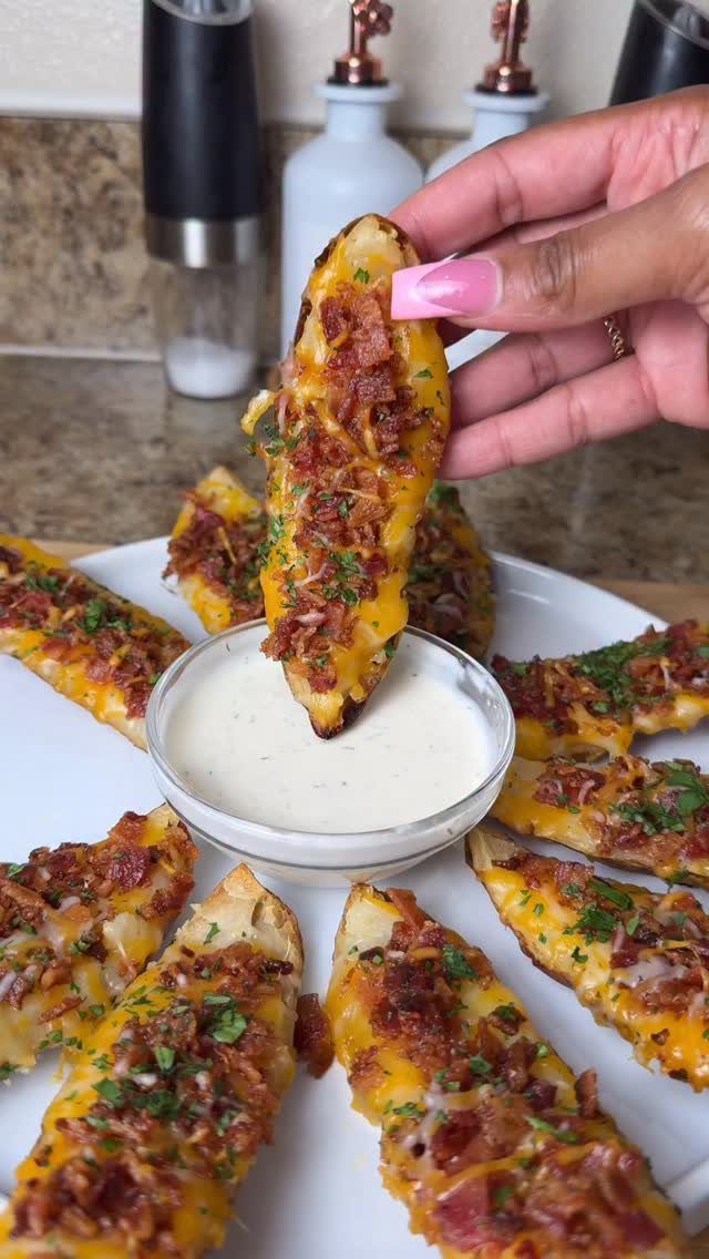Loaded potato skins with cheese and bacon being dipped into white sauce.