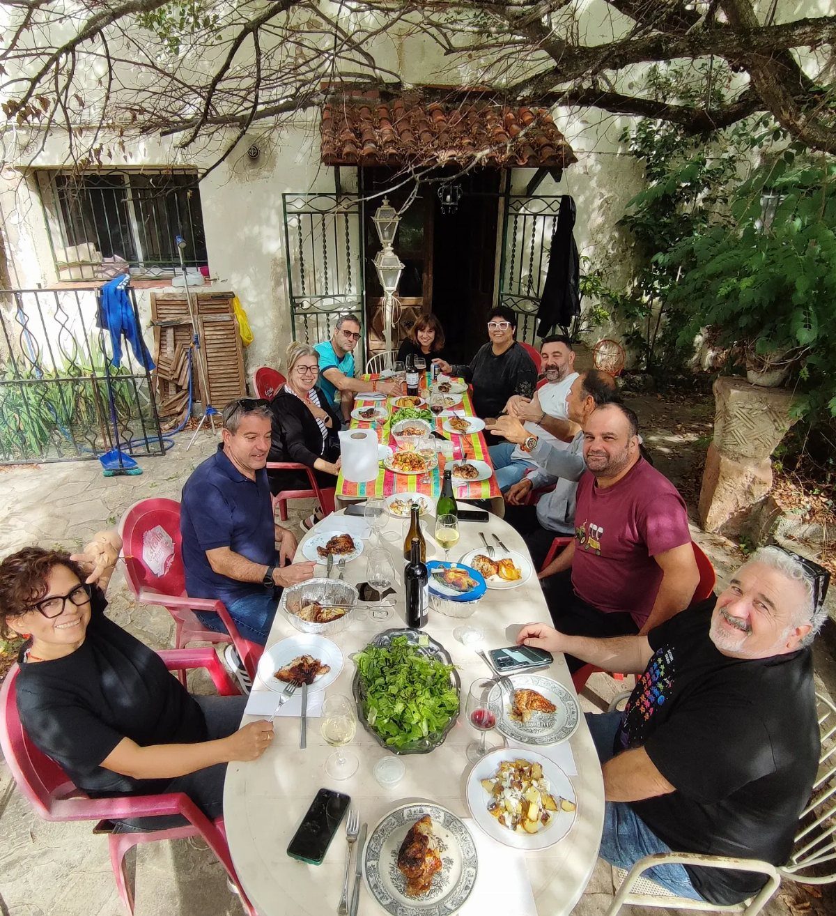 Group of people dining at long tables on an outdoor patio under trees.