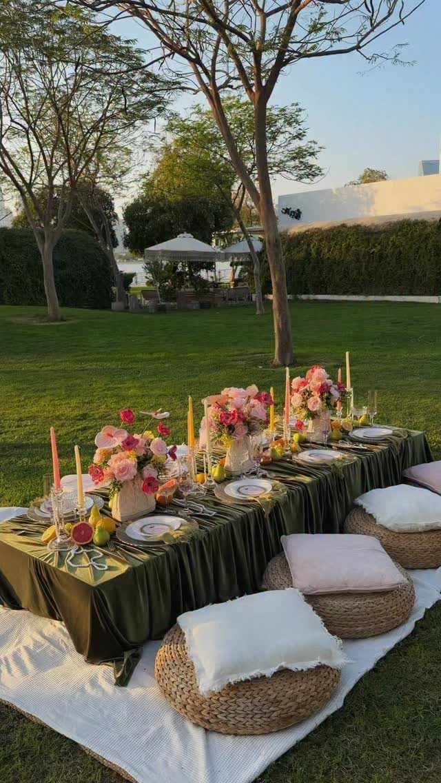 Outdoor dinner table set with flowers and candles on a lawn with pouf seating