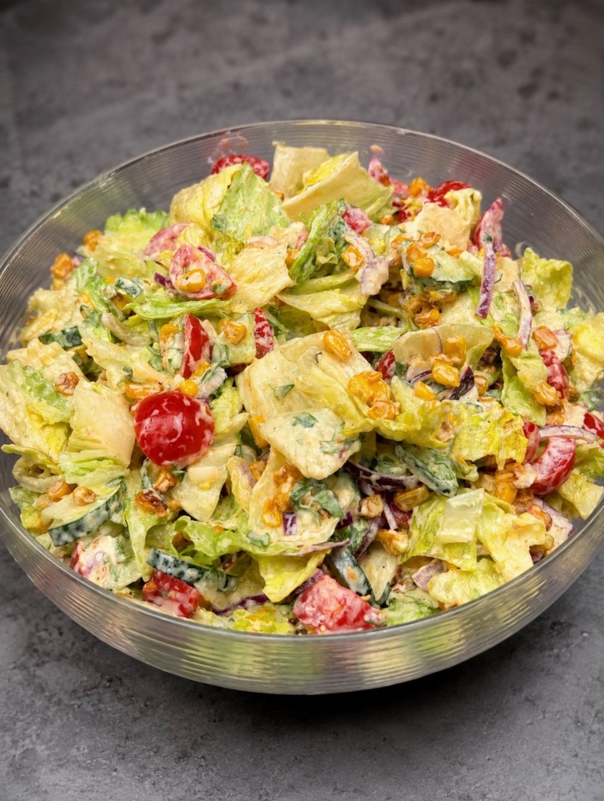 Mixed salad with corn and tomatoes in a clear glass bowl.
