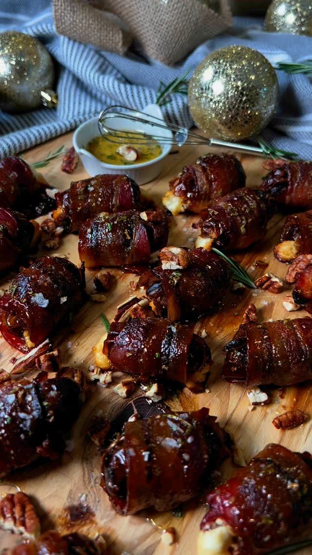 Bacon-wrapped dates on a wooden board with dipping sauce and gold ornaments.