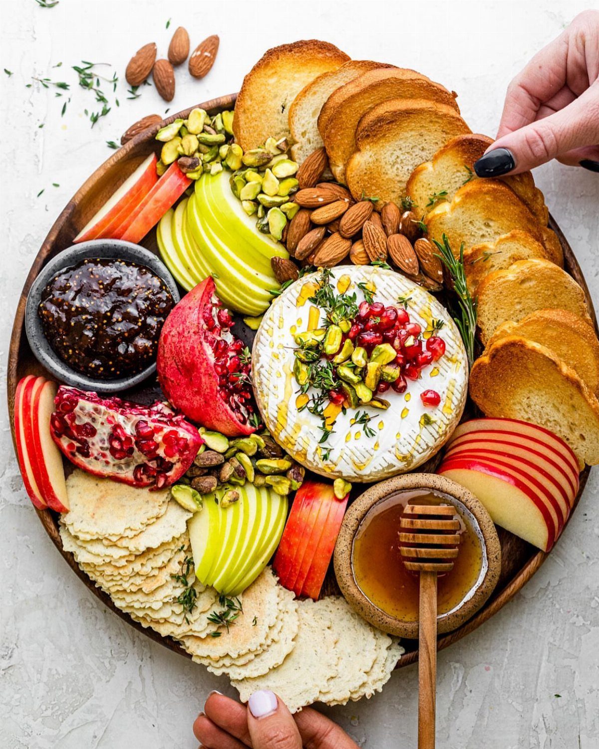 Baked brie topped with pistachios and pomegranate on a platter with fruit and crackers