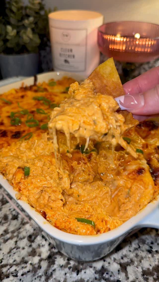 Buffalo chicken dip in a white dish with a chip scooping out cheese.