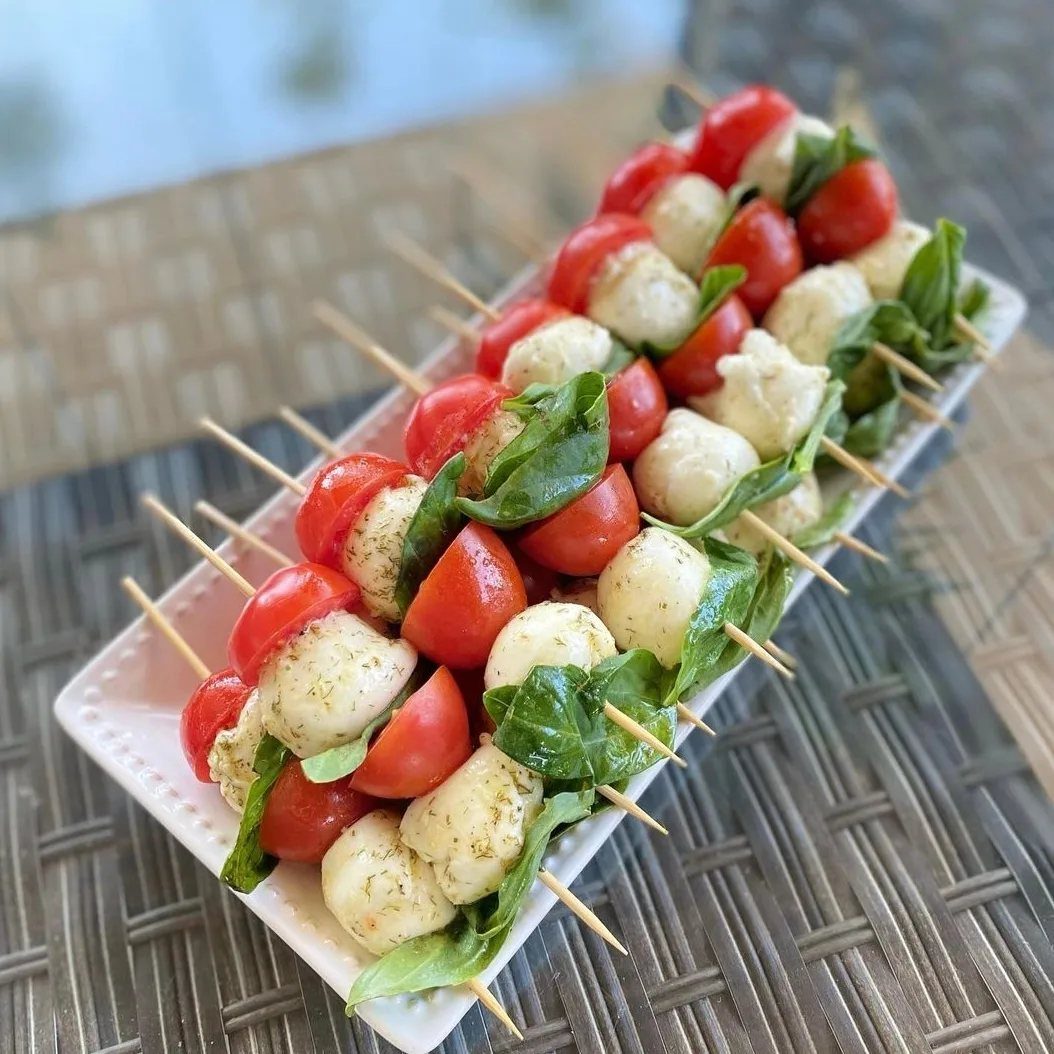 Caprese skewers with cherry tomatoes, mozzarella balls, and basil on a white platter.