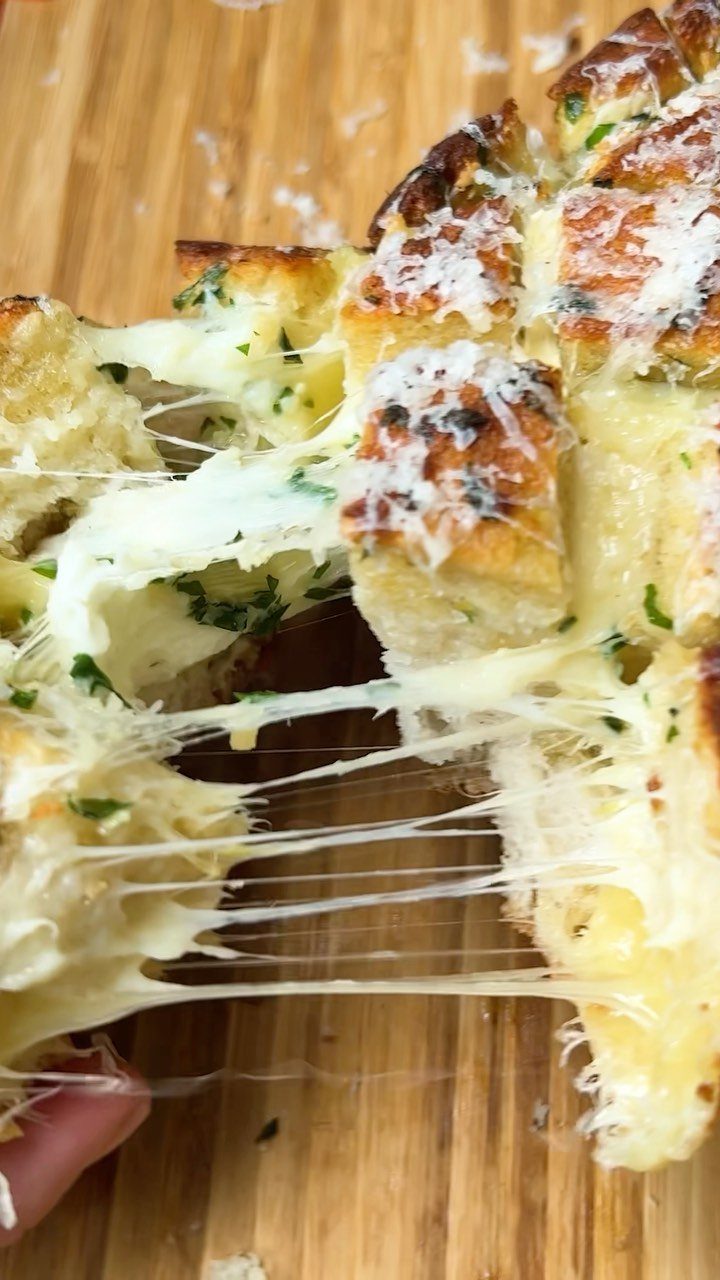 Cheesy garlic bread with melted cheese pull on a wooden cutting board
