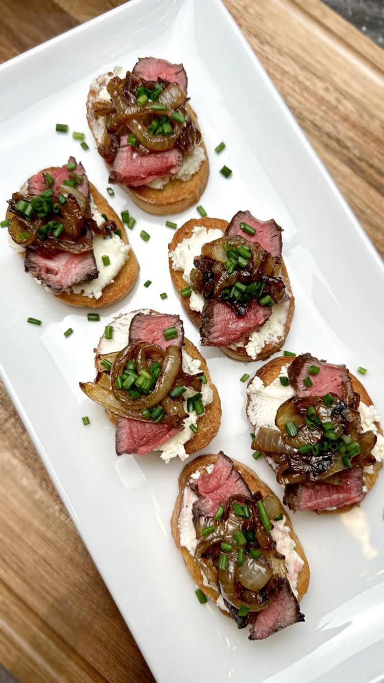 Steak and caramelized onion crostini with cream cheese on a white platter.