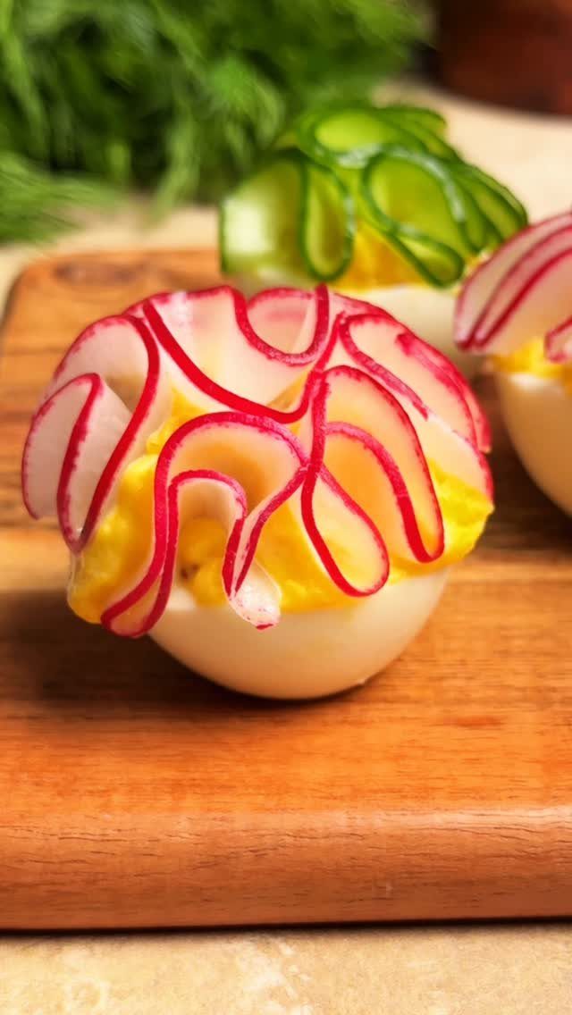 Deviled eggs topped with curled radish and cucumber slices on a wooden board.