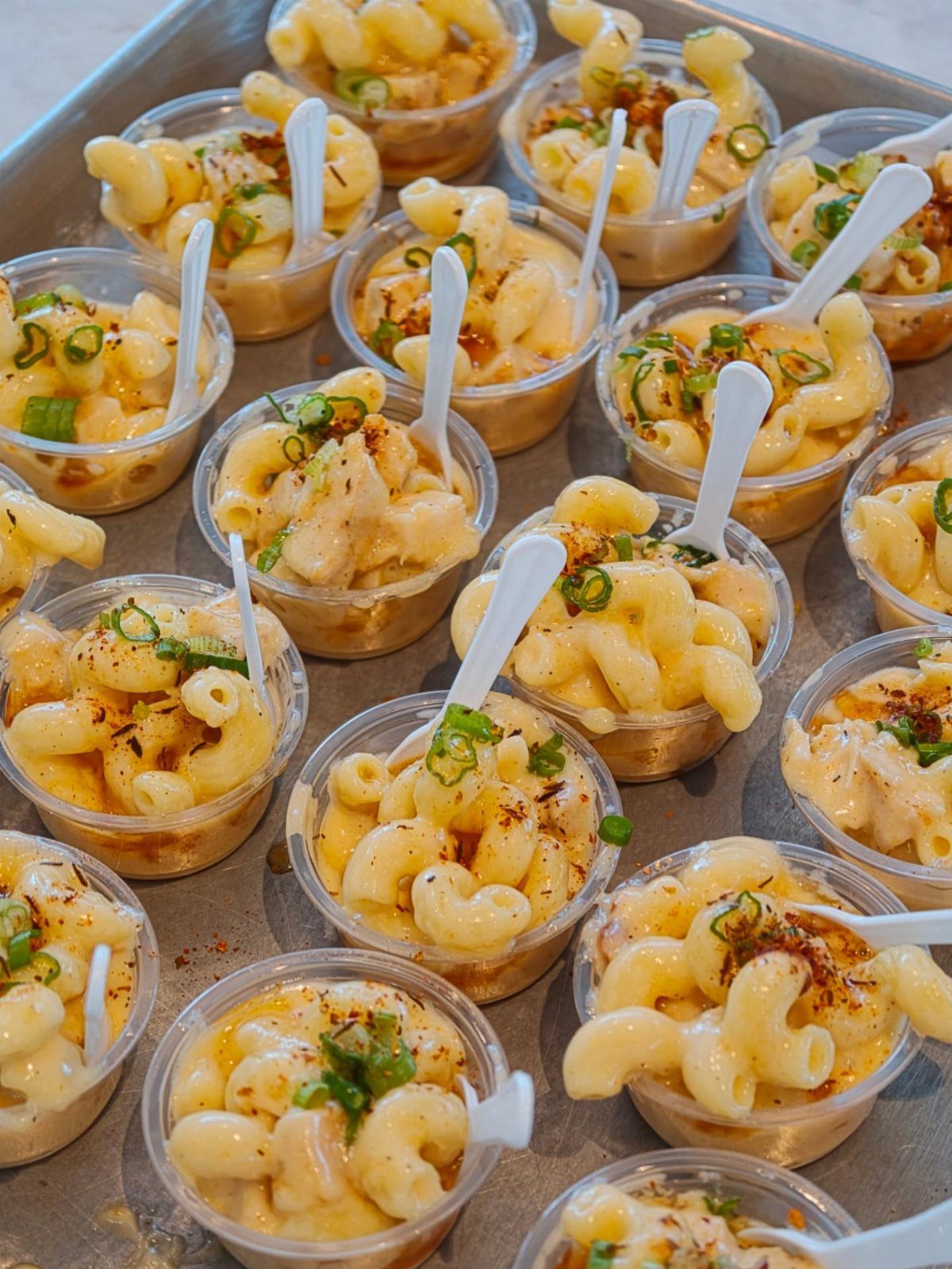 Macaroni and cheese served in small plastic cups with spoons and green onions.