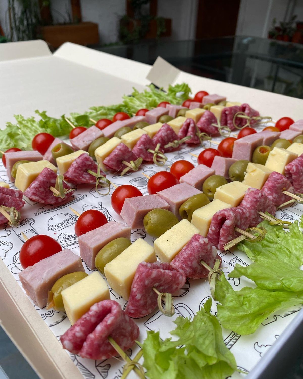 Meat and cheese skewers with olives and cherry tomatoes on a white tray.