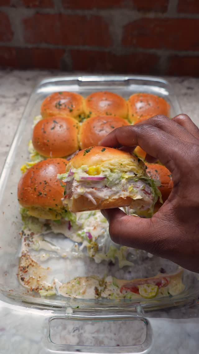 Mini sliders with coleslaw in a glass baking dish, one held by hand.