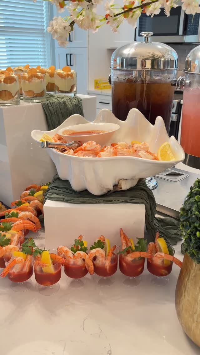 Shrimp cocktail served in a shell-shaped bowl and individual glasses on a buffet.