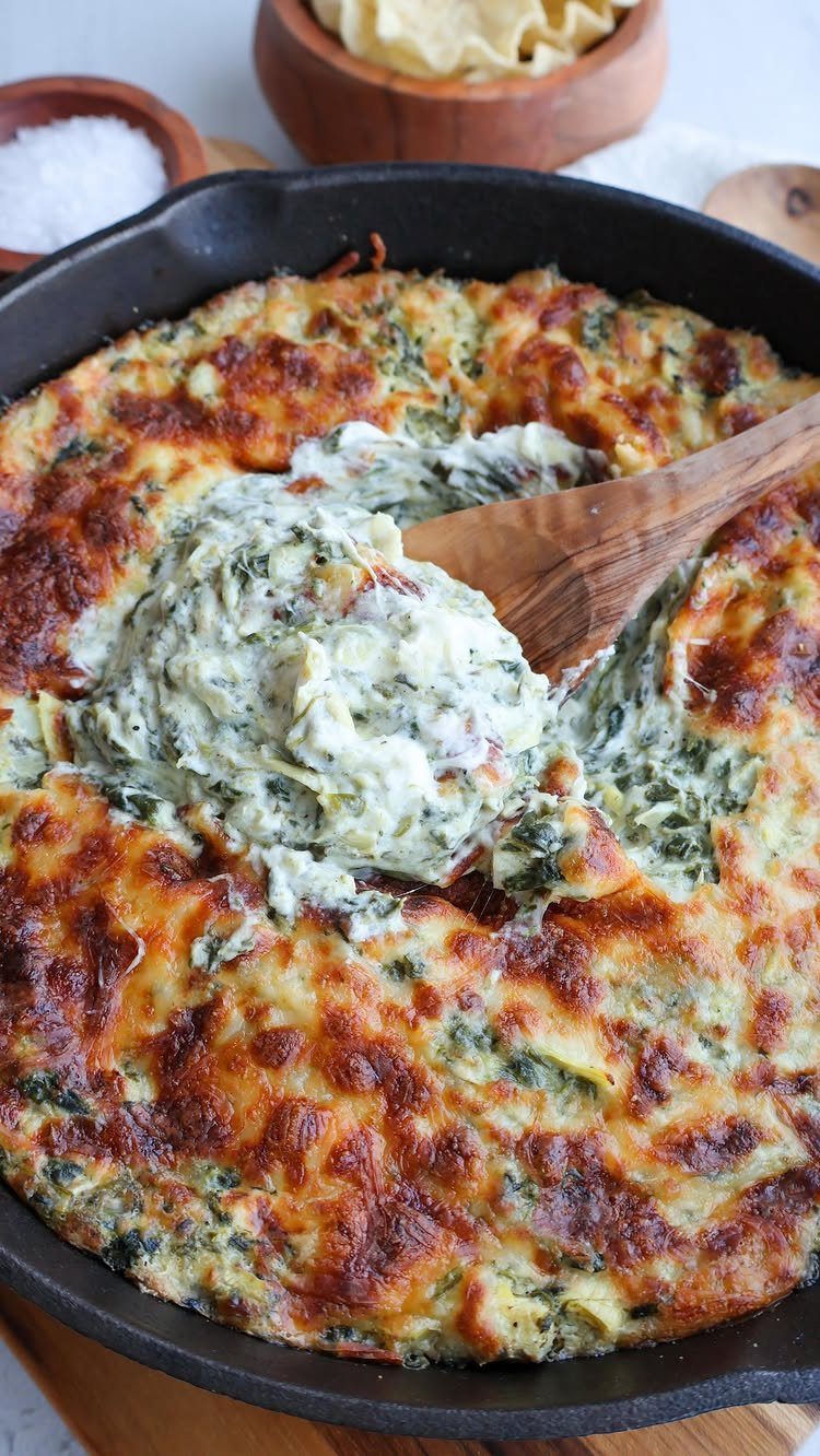 Spinach artichoke dip in a cast iron skillet with a wooden serving spoon.