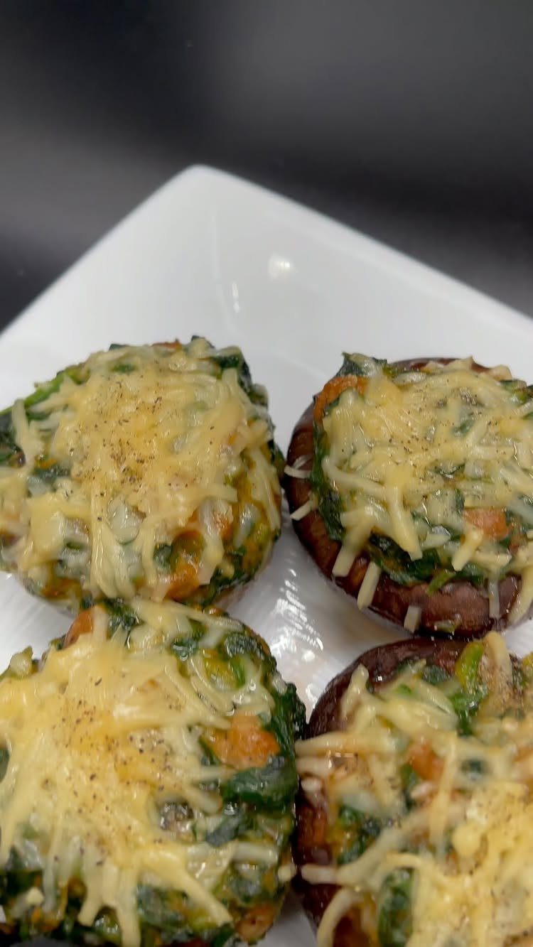 Stuffed mushroom caps with spinach and melted cheese on a white plate.