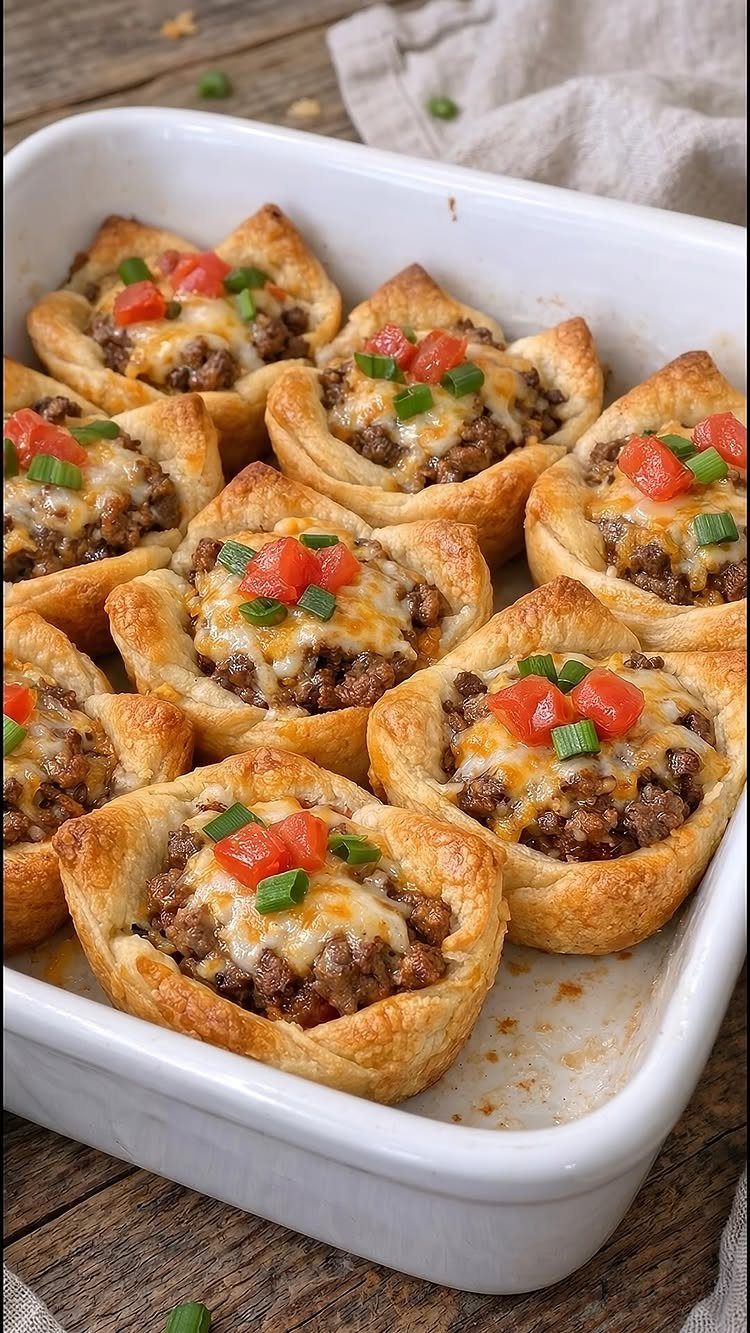 Pastry cups filled with taco meat and cheese topped with tomatoes and onions.